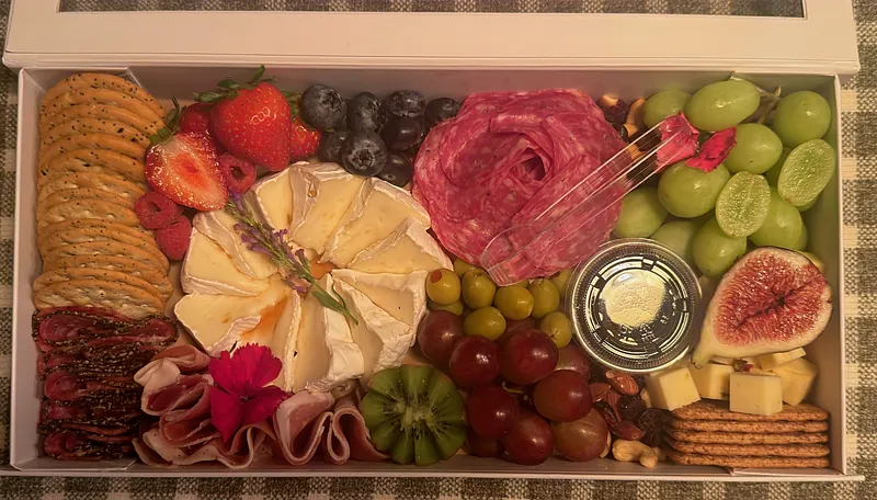 Charcuterie box with a petal-cut brie wheel, salami rose, prosciutto, fresh figs, grapes, olives, berries and crackers