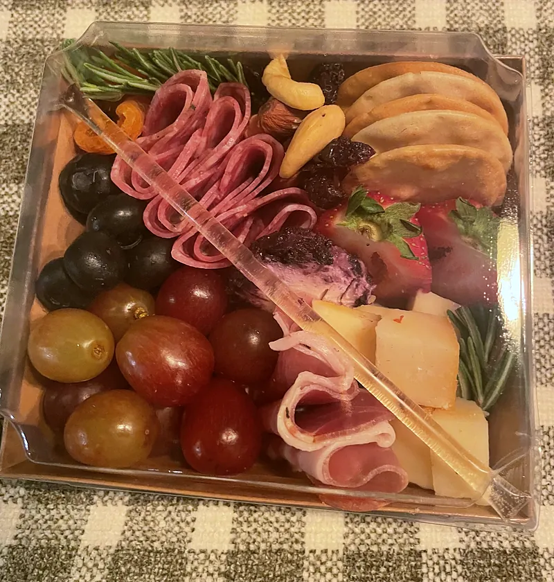 Individual charcuterie box with folded salami, prosciutto, cheese cubes, grapes, strawberries, nuts, crackers and rosemary